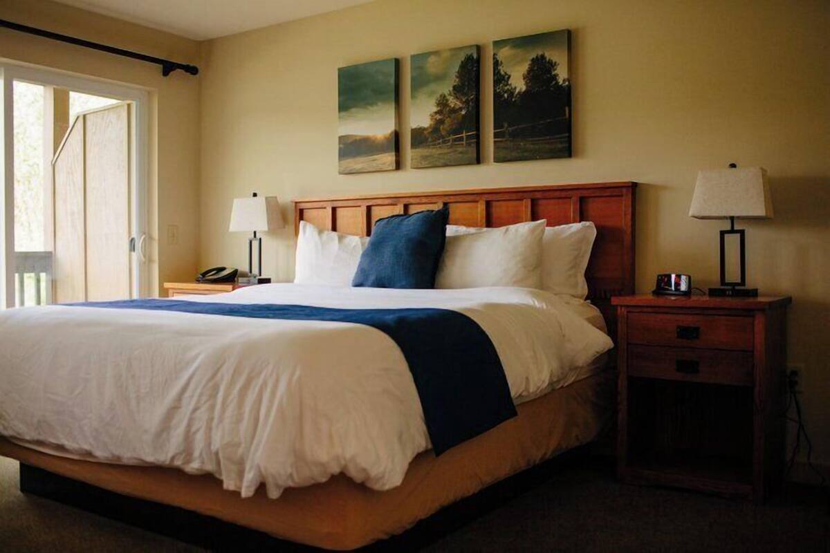 Una cama bien hecha con cabecera de madera, dos lámparas de noche y una mesita de noche con un teléfono.