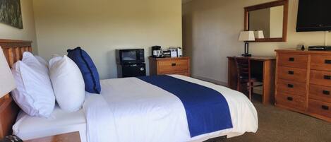 Een hotelkamer met een bed, een bureau met telefoon, een televisie, een dressoir en een schilderij aan de muur.