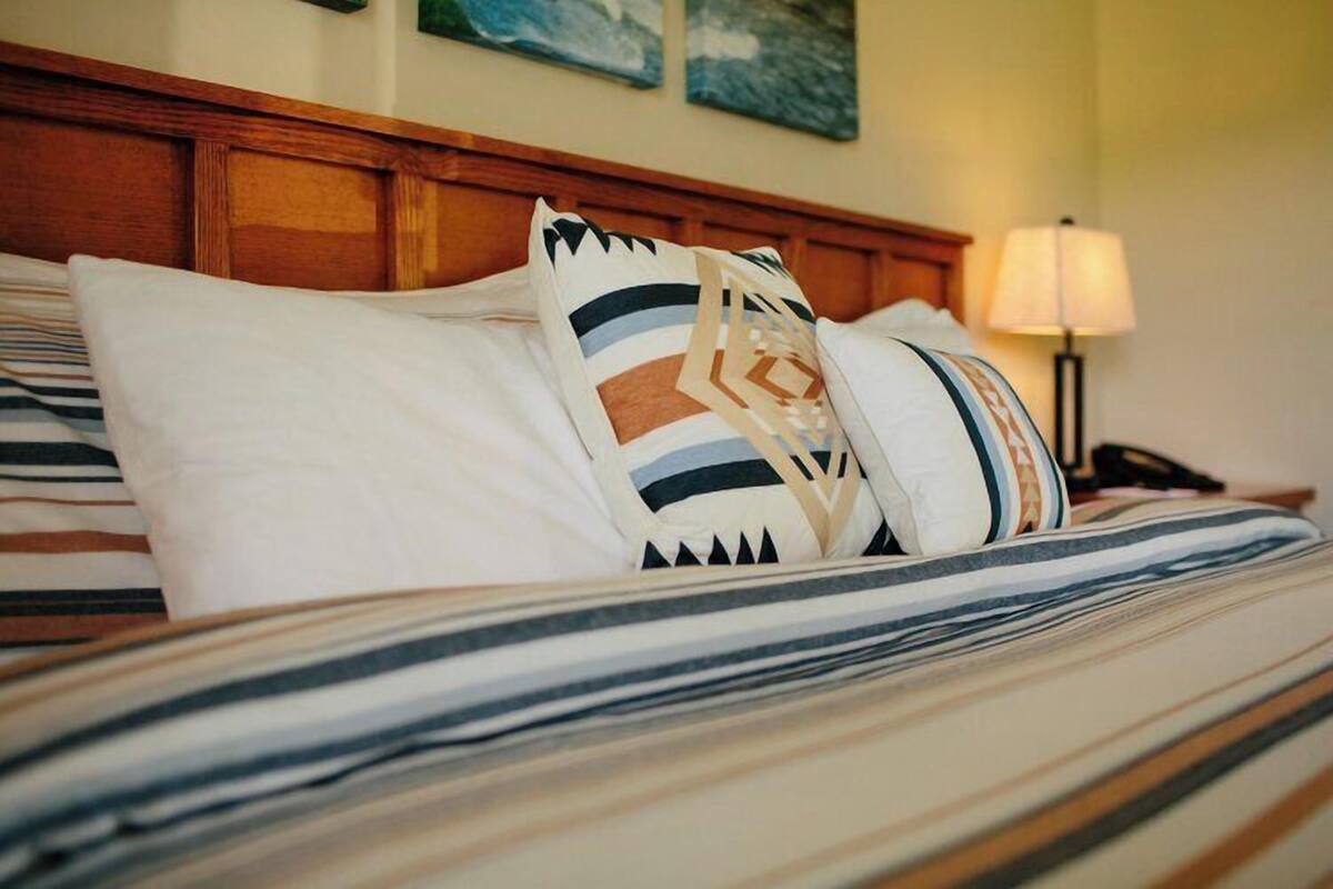 Una cama bien tendida con ropa de cama a rayas y almohadones decorativos.
