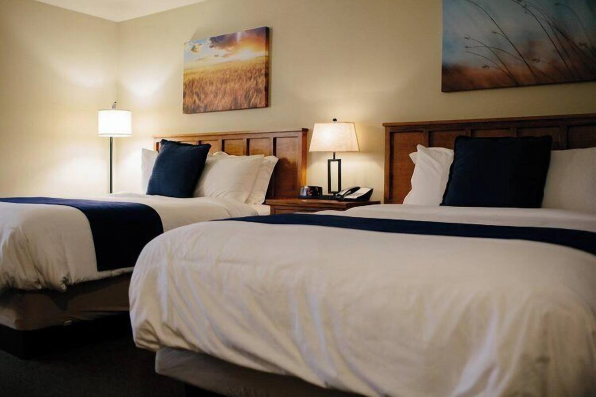 Habitación de hotel con dos camas, cada una con cabecero de madera, ropa de cama blanca y una mesita de noche con lámpara.