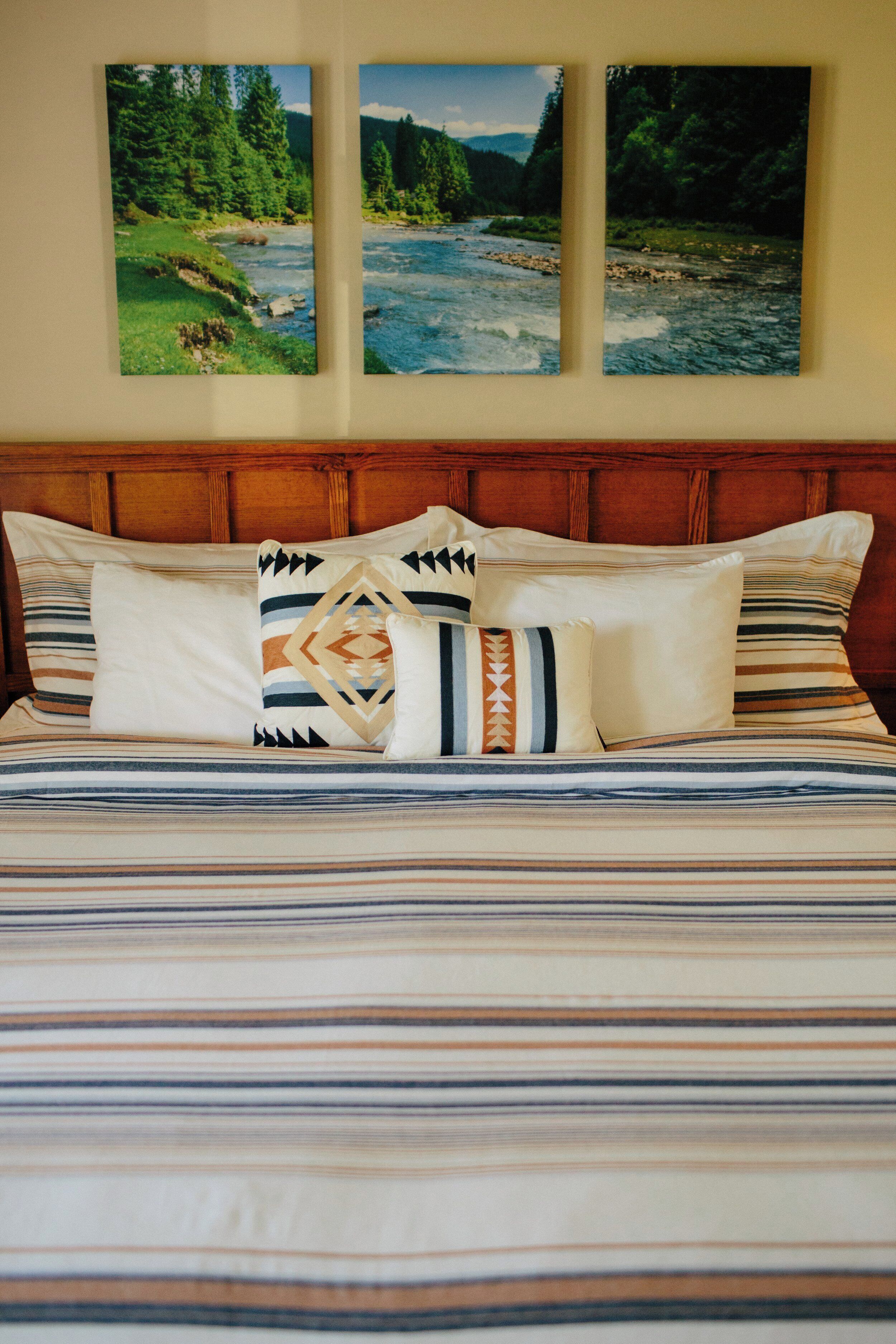 A bed with striped bedding, multiple pillows, and three framed landscape pictures on the wall.