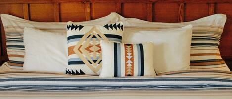 A bed with striped bedding, multiple pillows, and three framed landscape pictures on the wall.