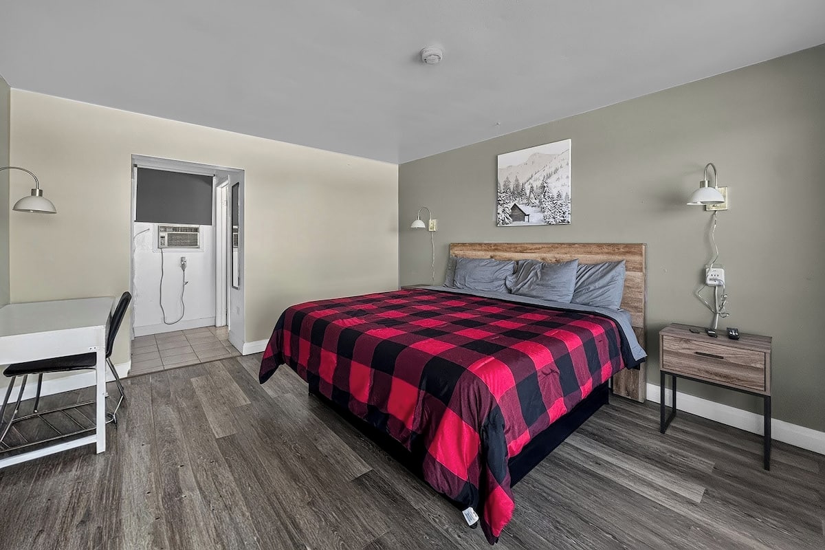 A bedroom with a bed, bedside tables, a desk, and a door leading to a bathroom.