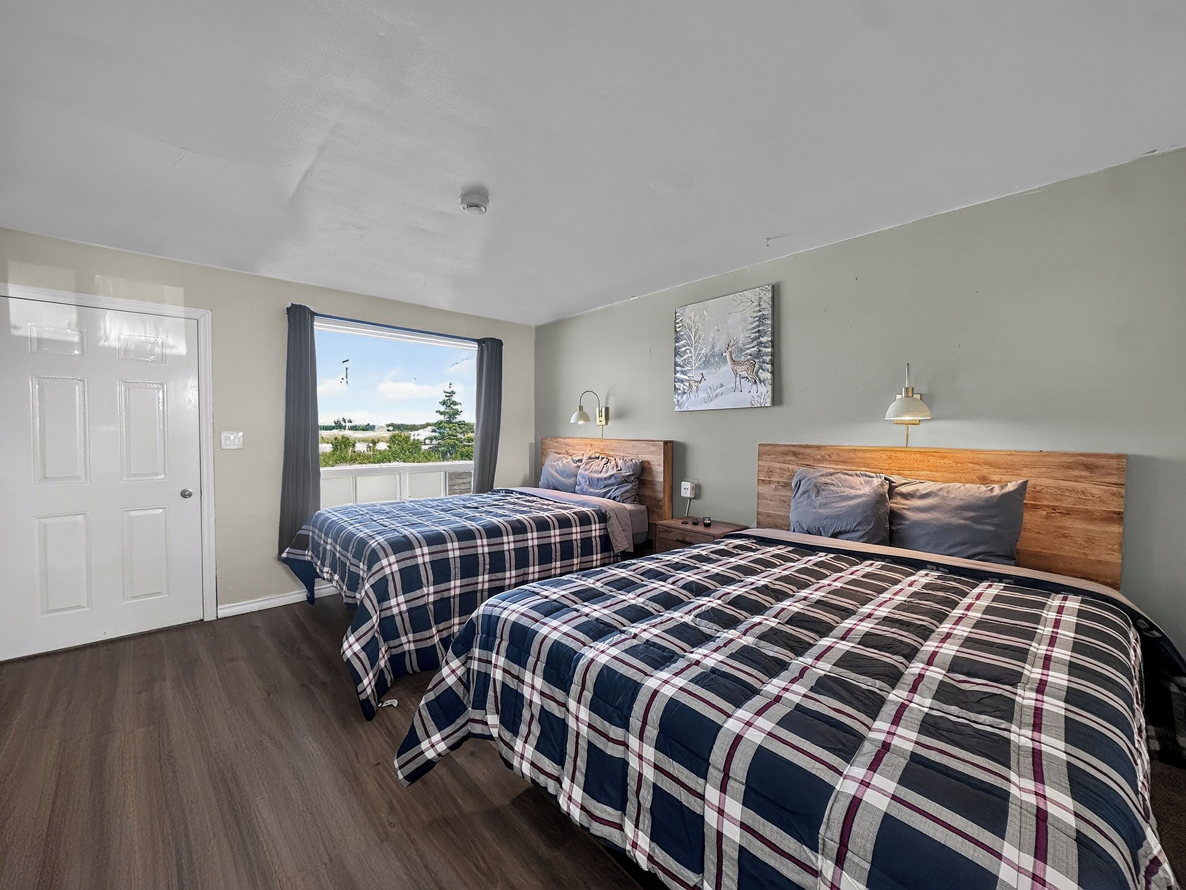 A bedroom with two beds, a window with a view, a door, and a ceiling light.