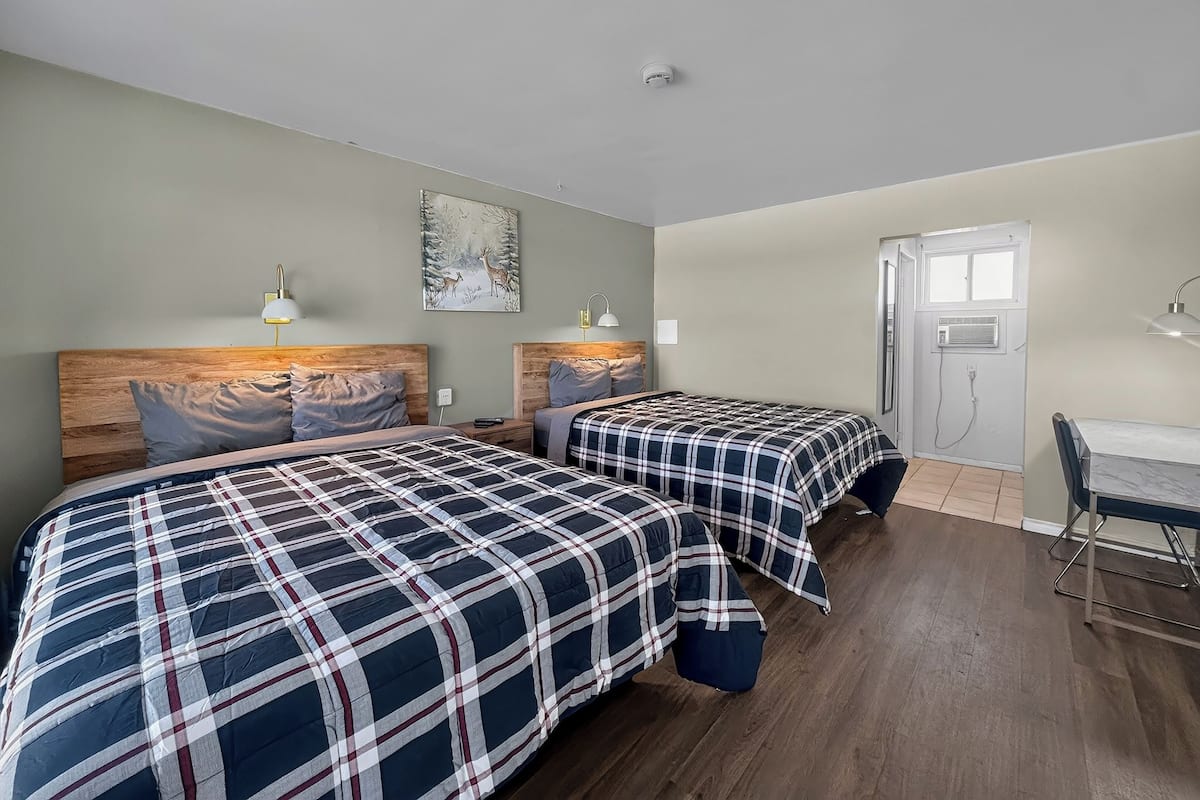 A room with two beds, a desk, and a door leading to a bathroom.
