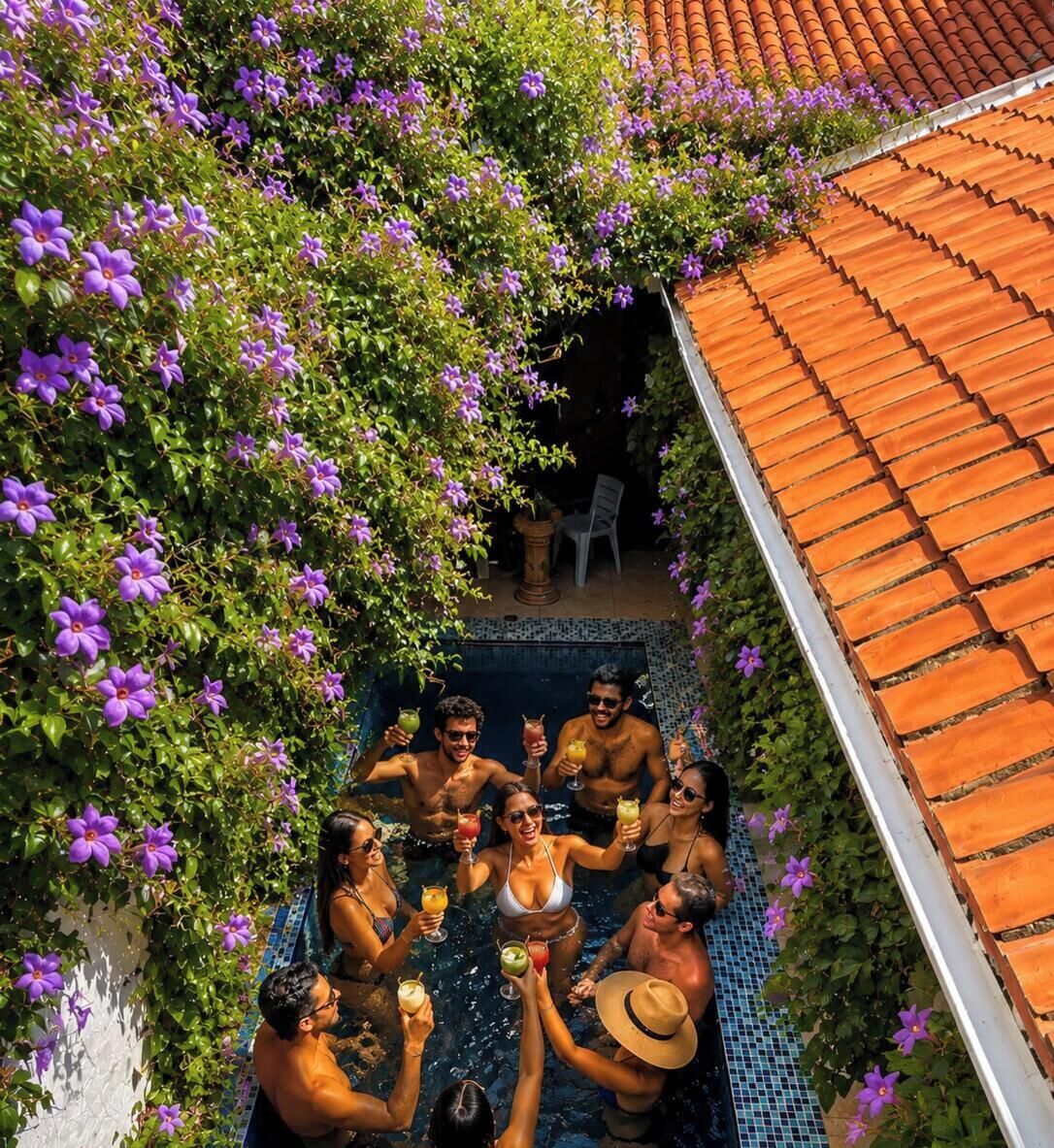 Un grupo de personas cerca de una piscina con techo de azulejos y un jardín con flores moradas.