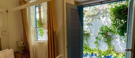 A bedroom with a four-poster bed, an air conditioning unit, a window with curtains, and an open door leading to a pool area.