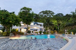 A pool area with lounge chairs and umbrellas, surrounded by lush greenery and a modern building. - Green9 Hotel & Beach Resort Same (Tonchigüe)