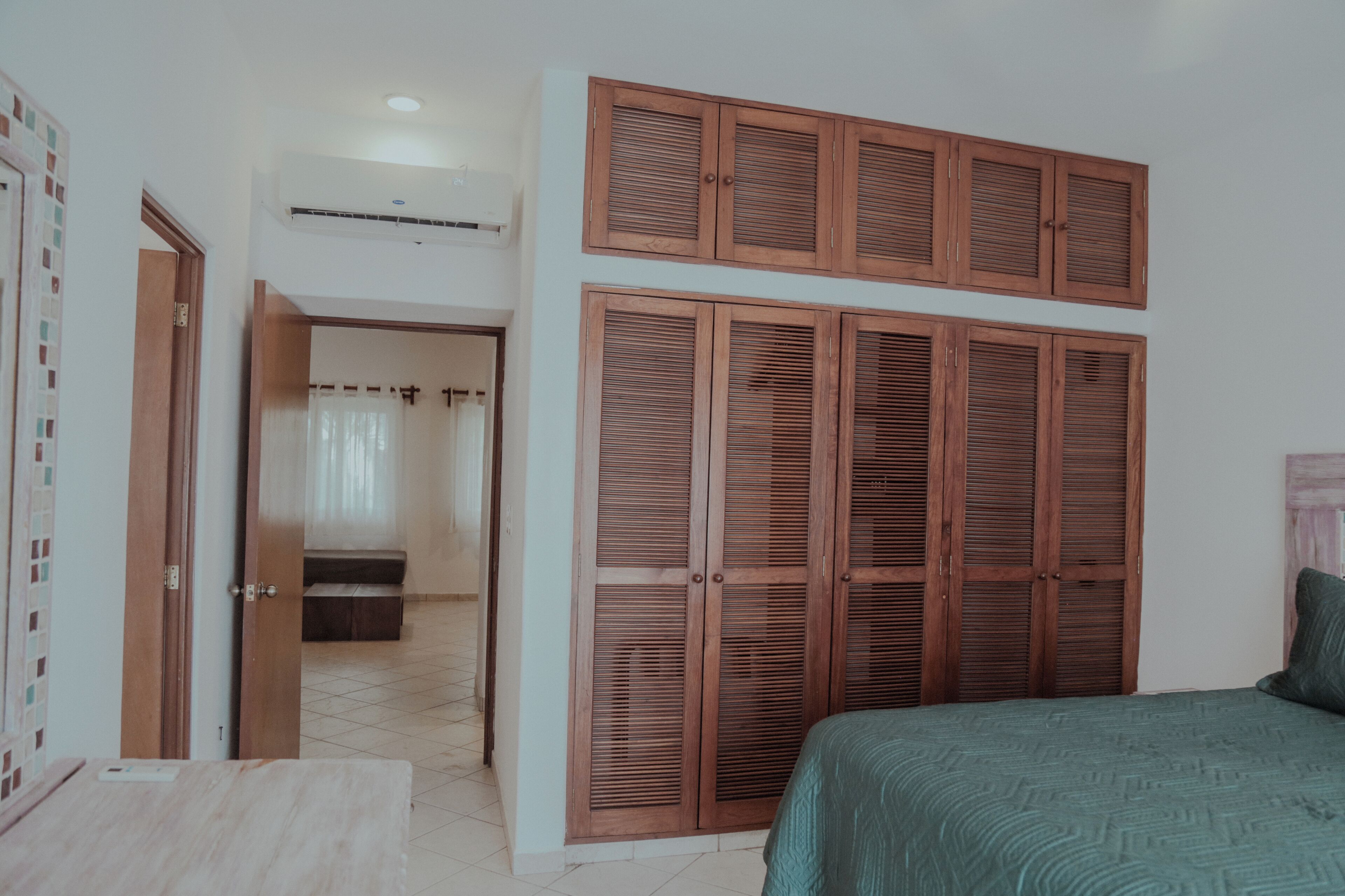 A bedroom with a bed, a wardrobe with louvered doors, and a bathroom visible through an open door.