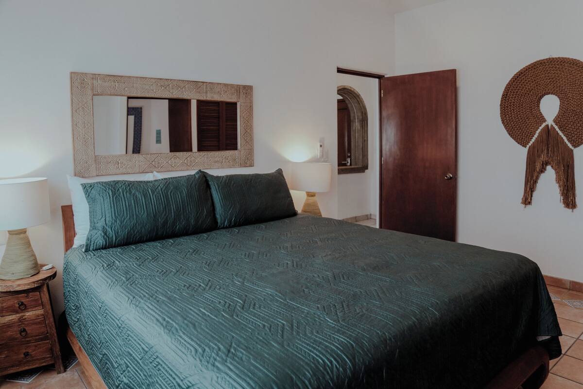Ein Schlafzimmer mit einem Bett, einem Nachttisch aus Holz, einem Spiegel und einer Tür.