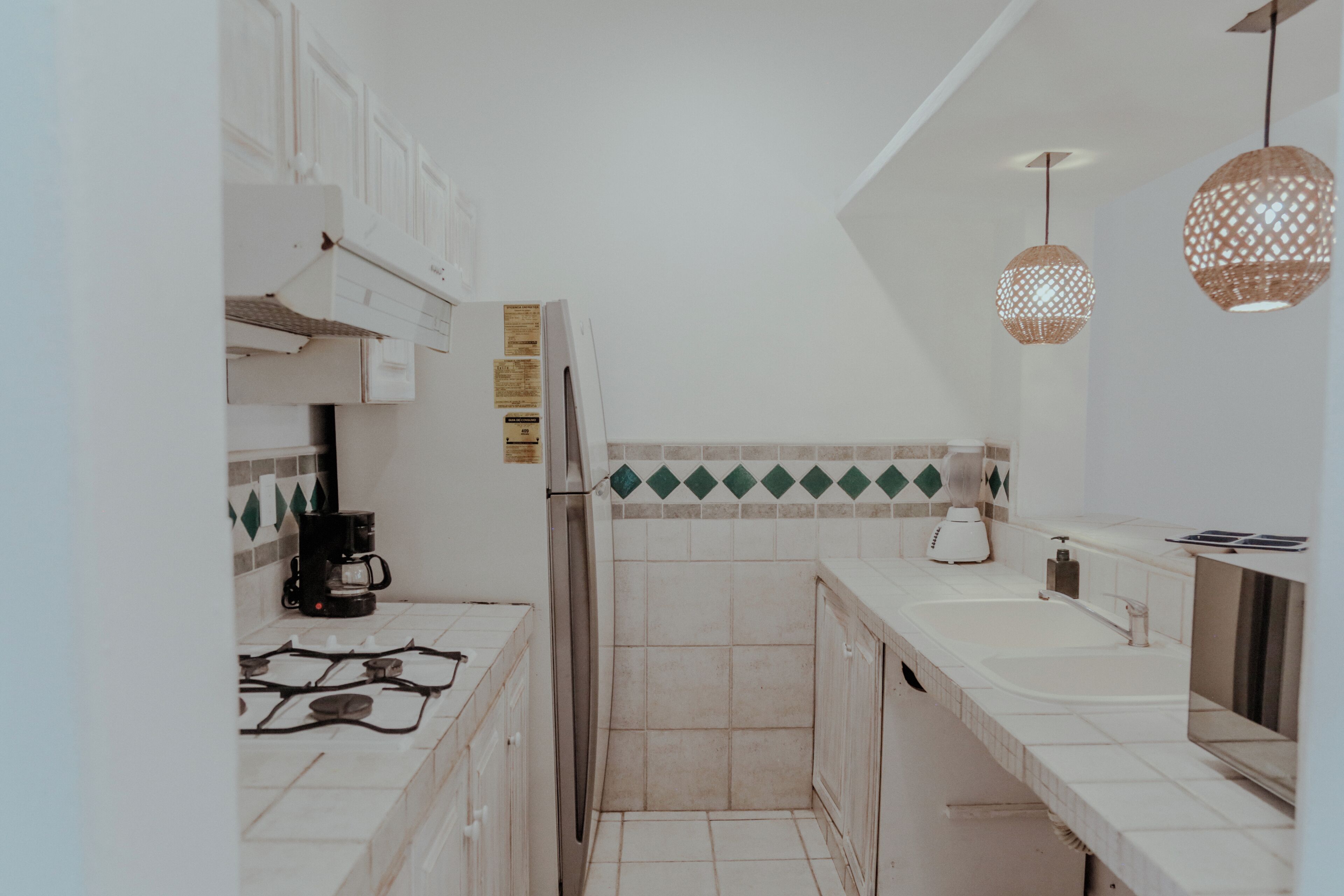 A kitchen with white cabinets, a gas stove, a coffee maker, and two hanging pendant lights.