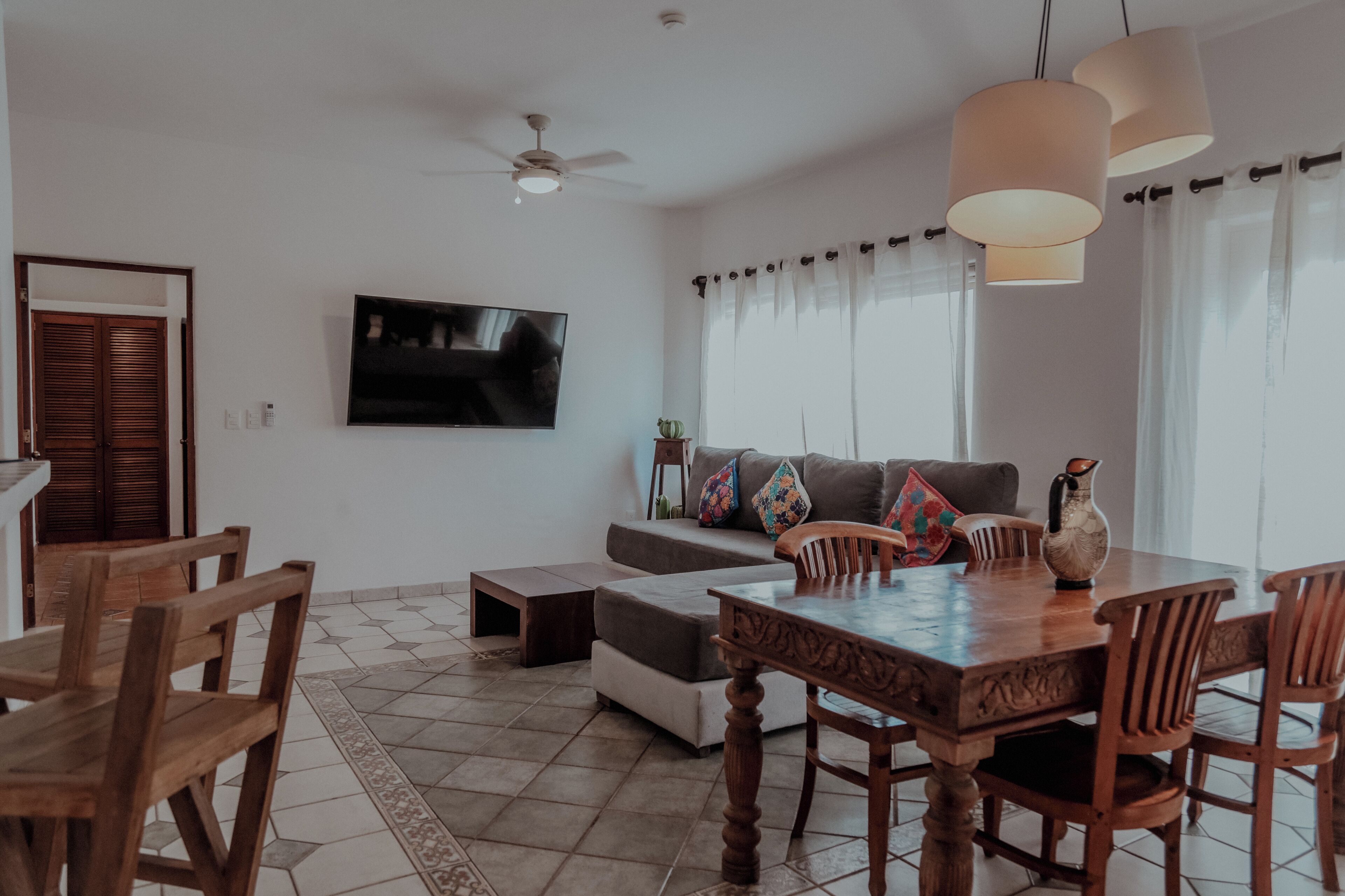 A modern living room with a wooden dining table, chairs, a sofa, and a television.