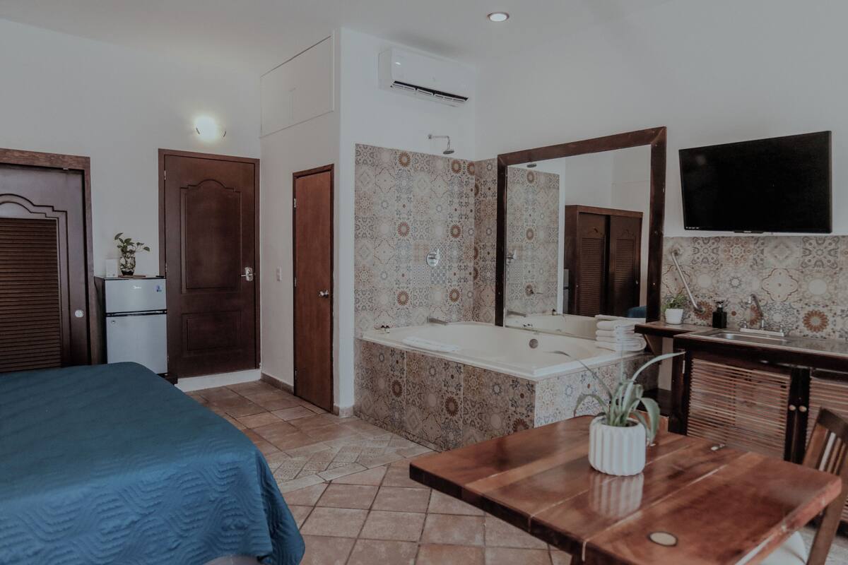 Ein Schlafzimmer mit Bett, einem kleinen Schreibtisch, einem Spiegel und einem Badezimmer mit Badewanne und Waschbecken.