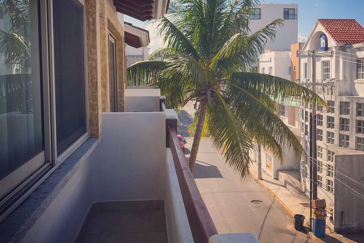 Ein Balkon mit Blick auf eine Palme und Gebäude.