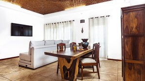 A dining area with a wooden table, chairs, a sofa, and a TV mounted on the wall. - Fabiola Condo Hotel (Playa del Carmen)