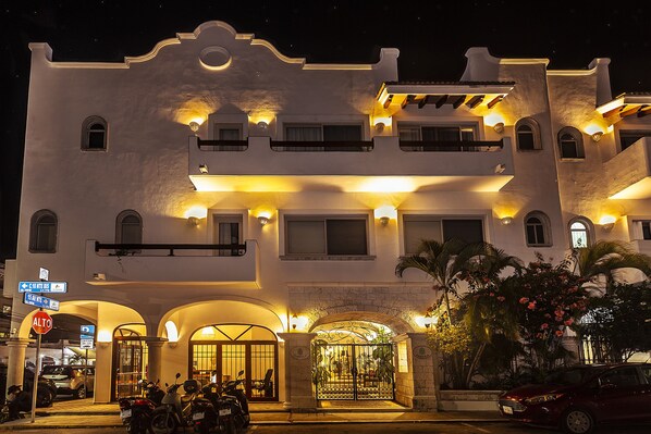 Un hotel con fachada blanca, varios balcones y una entrada protegida por una reja.