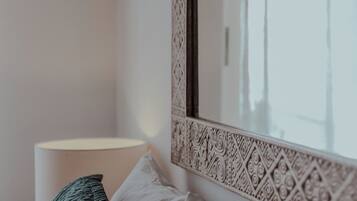 Un dormitorio con cama, almohadas, una lámpara y un espejo decorativo con un marco detallado.