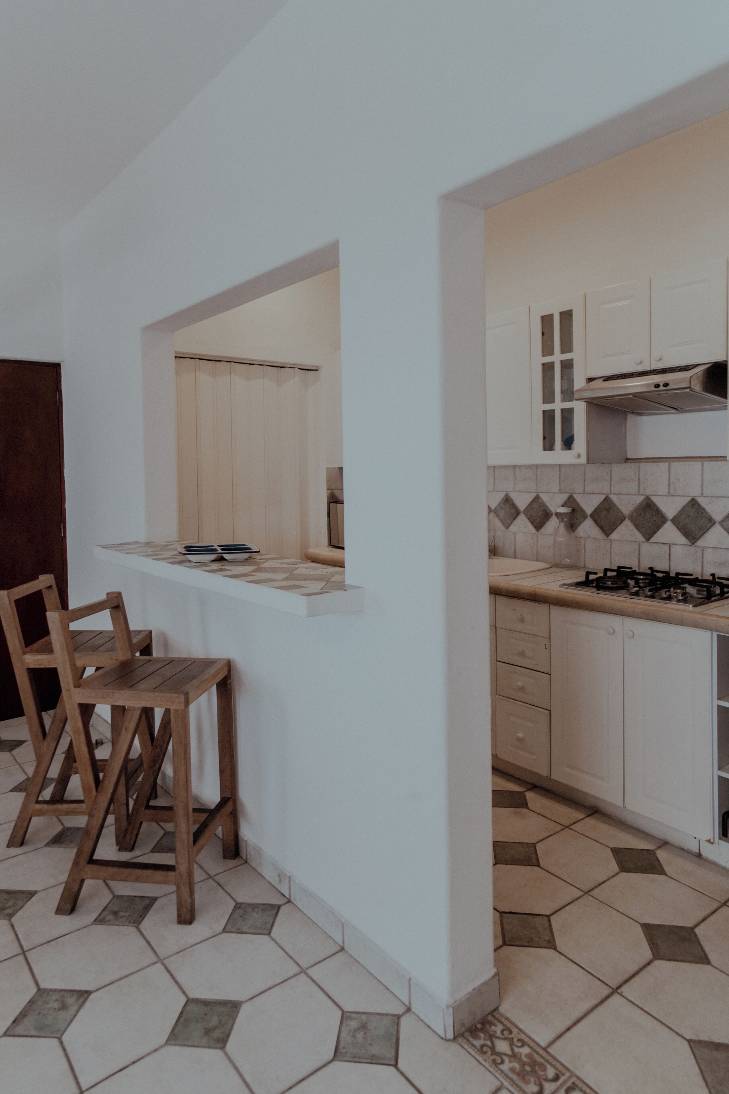 A kitchen with a central island, wooden chairs, and a tiled floor.