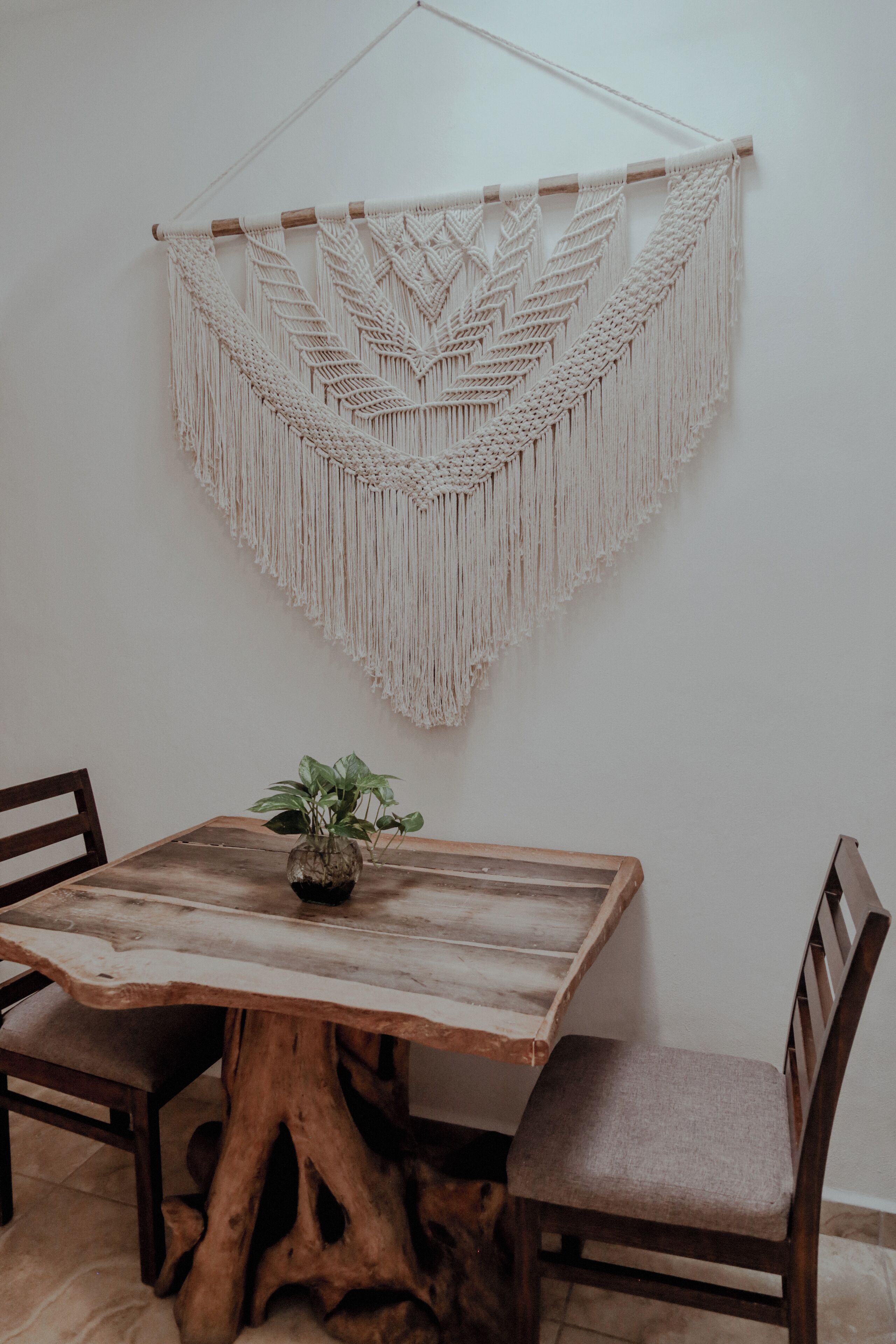 A dining table with a wooden base and a macrame wall hanging above it.