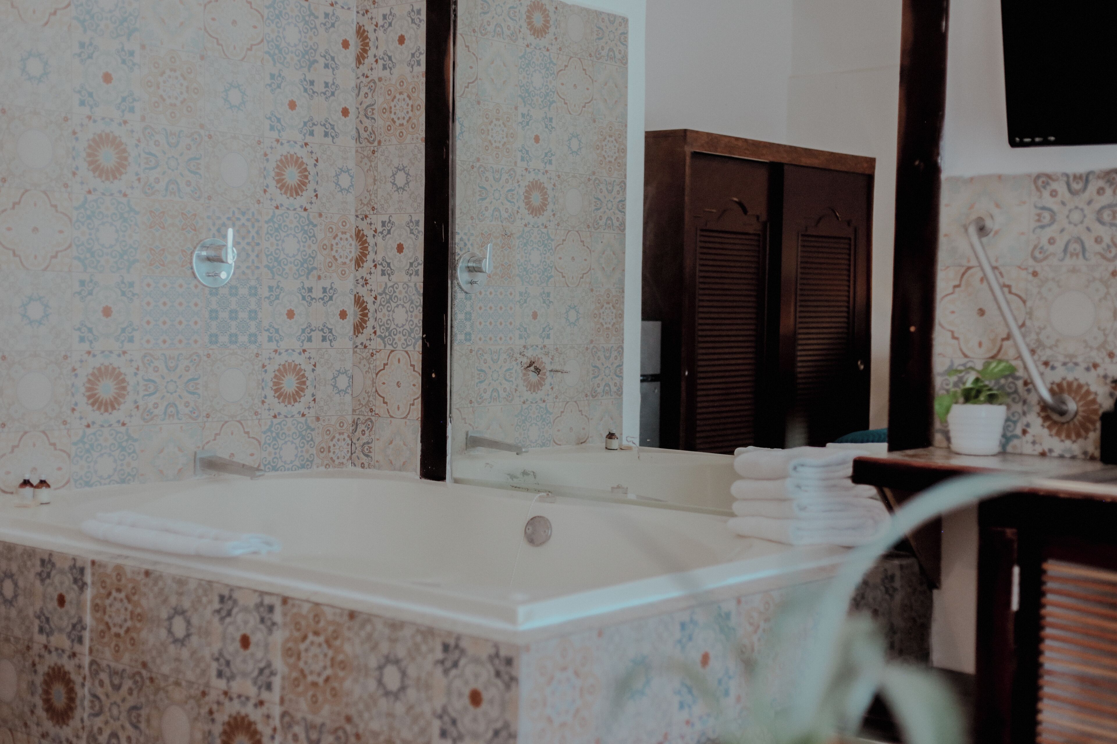 Un baño con una bañera grande, un espejo y baldosas estampadas.