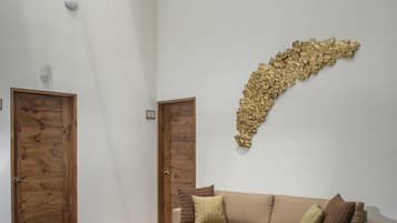 Una sala de estar con un sofá color beige, una mesa de centro de vidrio, una alfombra estampada y puertas de madera.