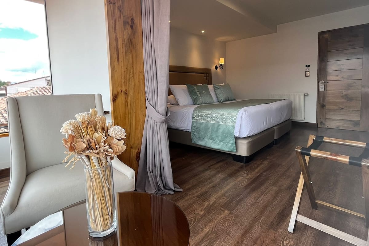 A hotel room with a bed, a chair, a table, and a view of the outside.
