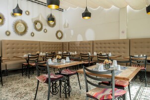 Un restaurante con una larga banca acolchada, mesas de madera y sillas negras.