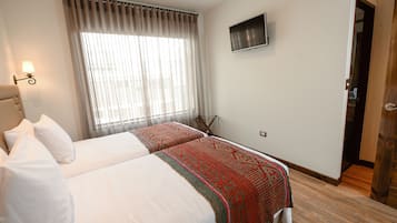 A hotel room with two beds, a TV mounted on the wall, and a large window with curtains.