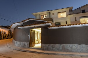 Una casa moderna de dos pisos con fachada de piedra, un balcón y un interior bien iluminado que se ve a través de la puerta abierta.