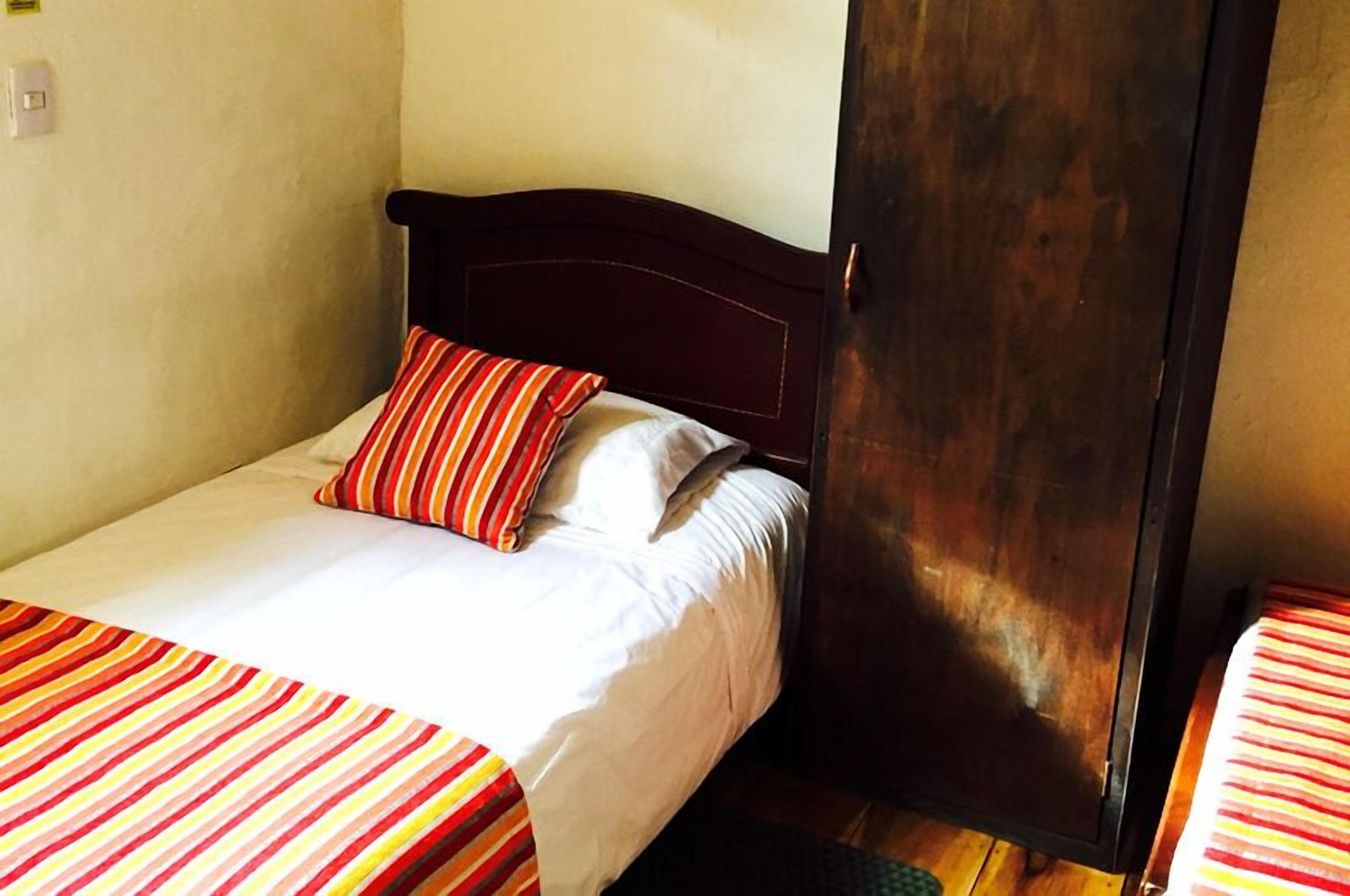 A single bed with a wooden headboard, white bedding, and striped red and yellow bedspread.