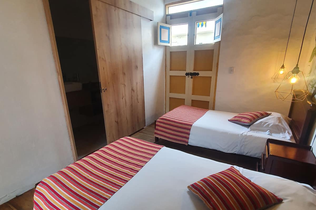 A room with two beds, wooden flooring, a wooden door, and a window with a view.