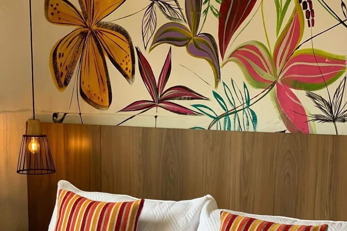 A bed with striped pillows and a striped blanket, a wooden headboard, and a wall with a floral mural.