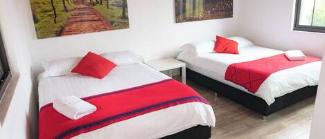 Une chambre d’hôtel avec deux lits, chacun agrémenté de draps blancs et de touches de couleur rouge, une petite table de chevet et une fenêtre.