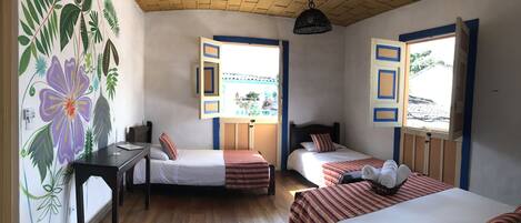 A room with two beds, a desk, and a window with an open shutter.