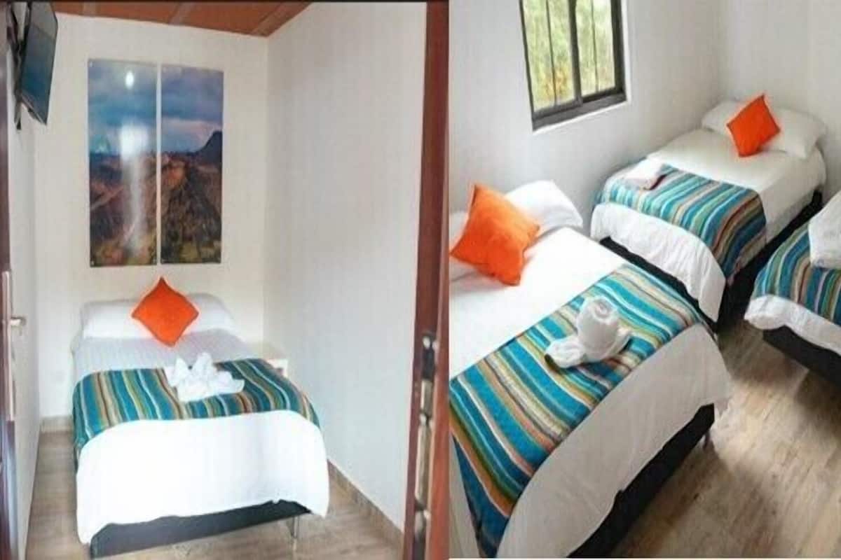 A hotel room with two single beds, each with striped bedding and orange pillows. There is a painting on the wall and a window with a view.