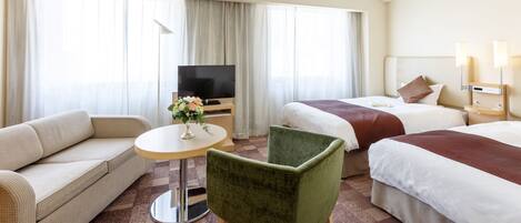 A hotel room with two beds, a sofa, a TV, and a small table with a vase of flowers.