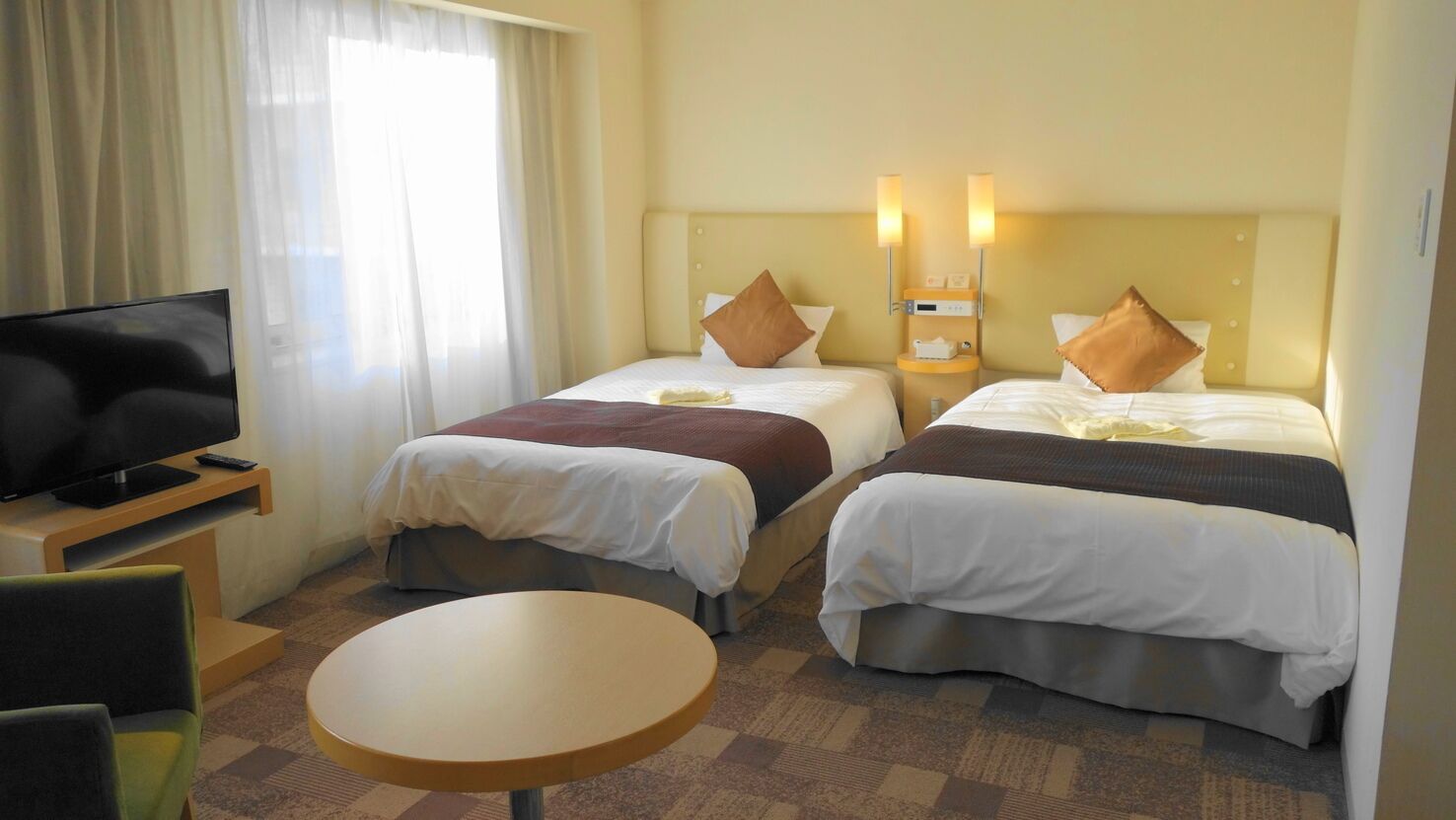 Une chambre d’hôtel avec deux lits, une télévision, une petite table et une fenêtre avec des rideaux.