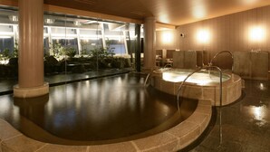 Un espace bien-être comprenant un jacuzzi, un sol en pierre et un mur de verre donnant sur un paysage verdoyant.