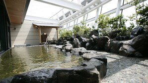 Un espace intérieur paisible agrémenté d’un élément aquatique, avec de gros rochers et une surface d’eau claire, le tout intégré dans un décor architectural moderne doté de grandes fenêtres et d’un plafond en bois.