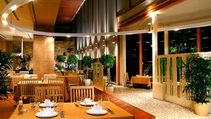 Un restaurant avec des tables dressées pour le service, des plantes en pot et une vue sur l’extérieur.