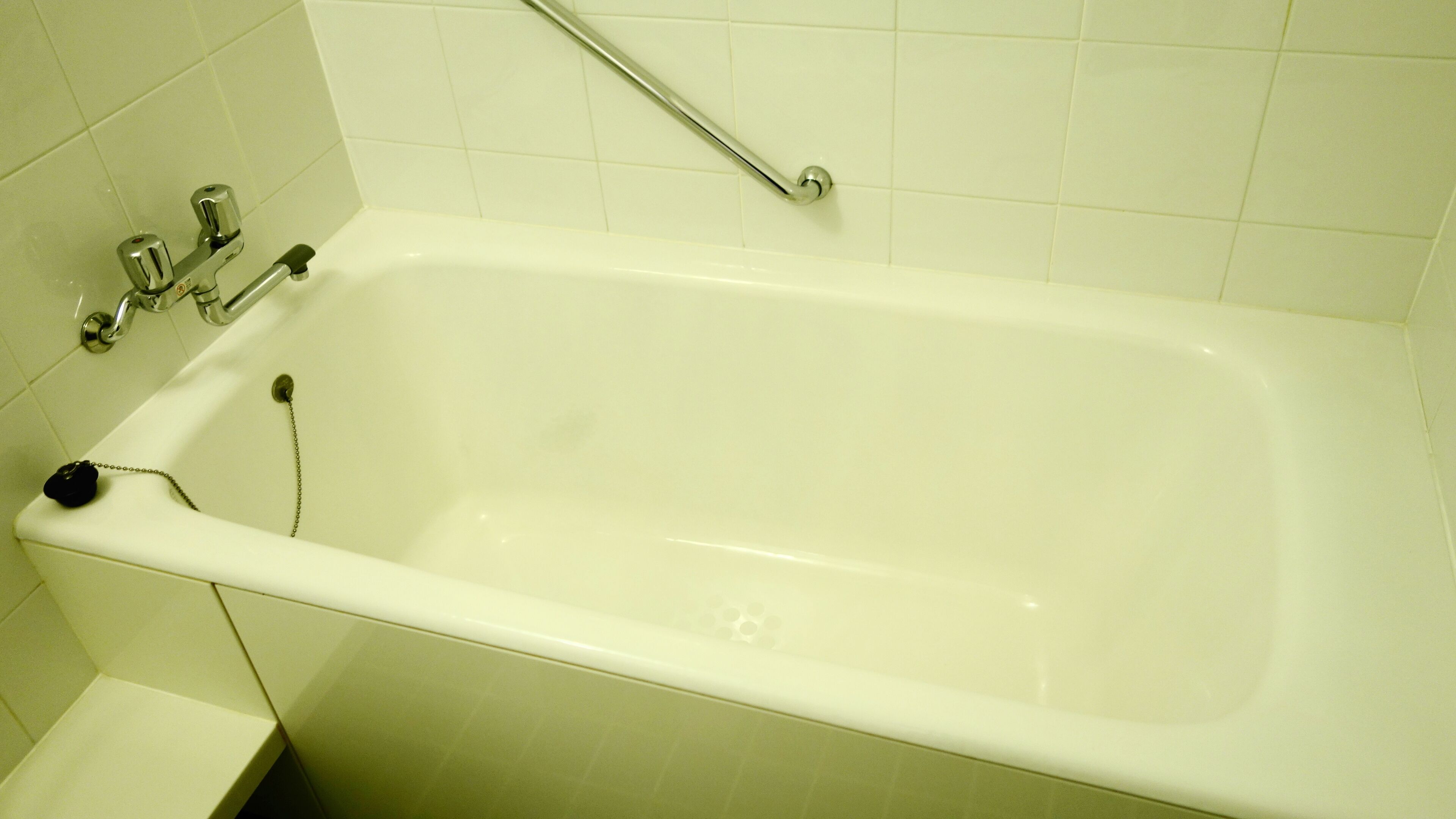 A standard white bathtub with a grab bar, a faucet, and a chain for safety.