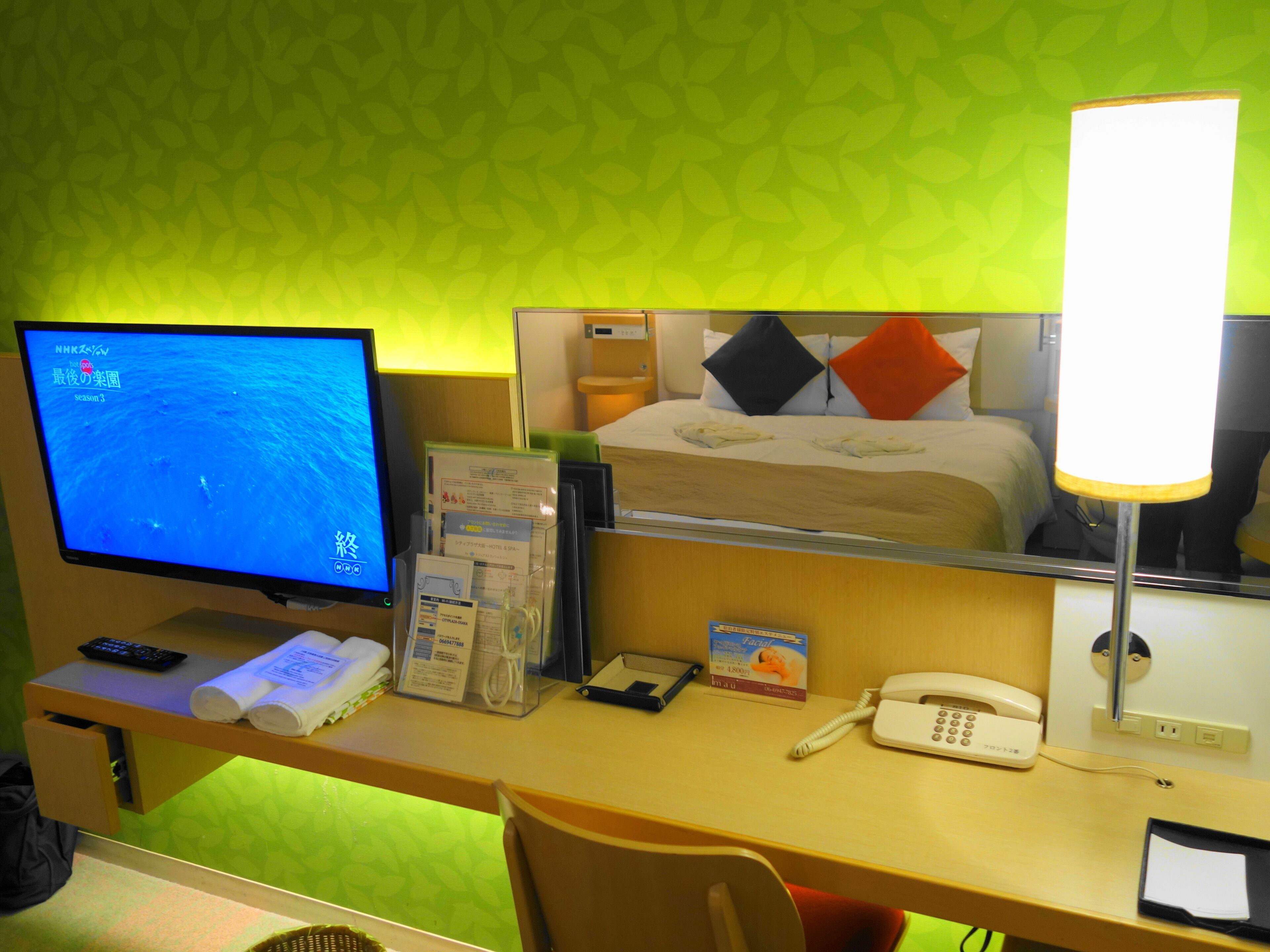 A hotel room with a bed, a desk with a computer, a phone, and a lamp.