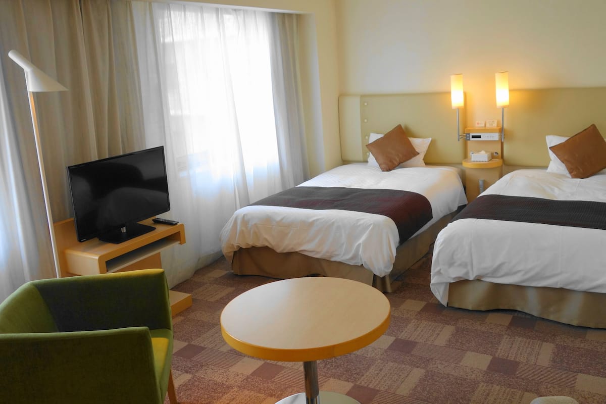 A hotel room with two beds, a TV, a table, and a chair.