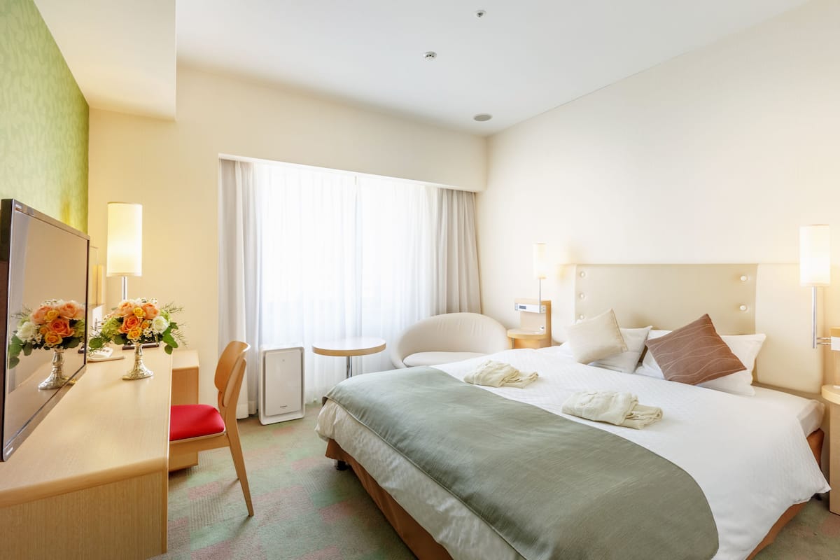 A hotel room with a bed, a desk with a chair, a small table, and a TV.