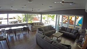 A spacious living area with sofas, a coffee table, and a dining table. There are ceiling fans and large windows providing natural light. - Global Backpackers - Port Douglas (Port Douglas)