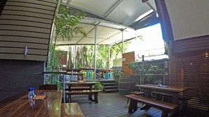 An outdoor dining area with wooden tables and benches, covered by a white canopy, surrounded by greenery and plants. - Global Backpackers - Port Douglas (Port Douglas)