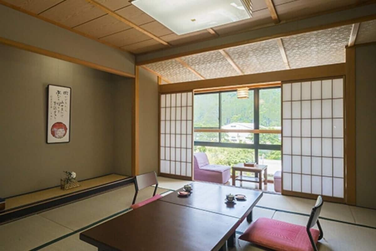 A traditional Japanese room with tatami flooring, a low table with a cushion, a sliding door with a view, and a small table with a chair.