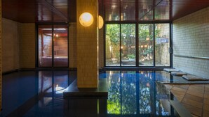 An indoor swimming pool with a wooden ceiling, large windows, and a view of greenery outside. - Suzuya Konnichiro (Kaga)