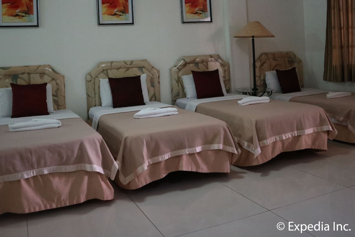 A hotel room with four beds, each with a headboard and pillows. There are three framed pictures on the wall.