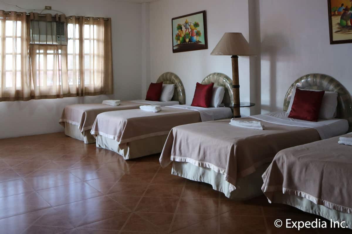 A hotel room with four beds, a ceiling fan, a window with curtains, and a painting on the wall.